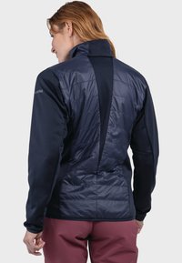 Marineblaue Jacke mit gesteppter Rückseite, weichen Stoffärmeln, hohem Kragen und integriertem Reißverschluss. Verfügt über ein kontrastierendes Design auf dem Rückenteil.
