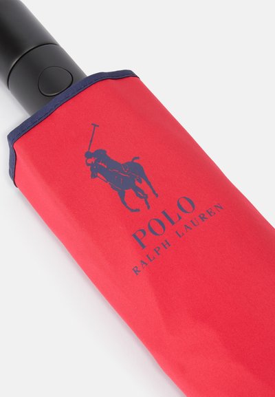 Manga de guarda-chuva vermelha com acabamento azul-marinho, apresentando um gráfico de logotipo e o texto "POLO RALPH LAUREN." Cabo preto mate visível na abertura.