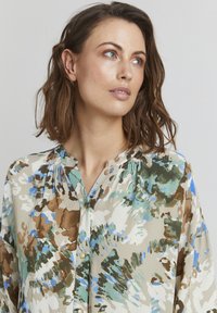 Flödande, flerfärgad blus i mjukt material med gröna, blå och bruna abstrakta mönster, med knäppning fram och svarvad halsringning.