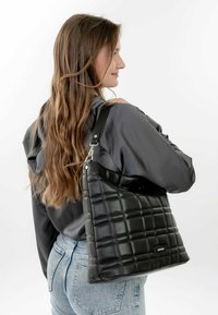 Black quilted leather handbag with a shoulder strap, showcasing a textured surface and a unique pattern.