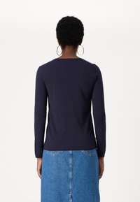 Ναυτική μπλούζα με μακρύ μανίκι από μαλακό ύφασμα με στρογγυλή λαιμόκοψη, συνδυασμένη με τζιν φούστα που διαθέτει πίσω τσέπες και ίσια γραμμή.