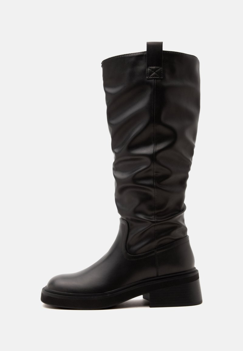 Botte haute en cuir noir avec tige souple et petit talon bloc, montrée de profil sur fond blanc.