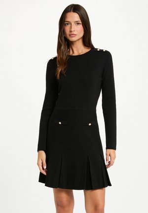Abito lungo nero con maniche, dal corpetto aderente e gonna a campana, caratterizzato da bottoni dorati decorativi sulle spalle e due tasche decorative.
