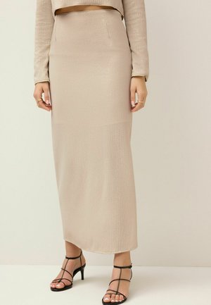 Beige ribbet lang nederdel med en glat tekstur og sideslids, parret med sorte stroppede hæl-sandaler. Minimalistisk design, tætsiddende silhuet.