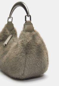 Kunstfell-Handtasche in gedämpftem Grün-Braun mit abgerundeter Form, ausgestattet mit einem dunkelmetallischen Griff und Lederakzenten. Weiche Textur.