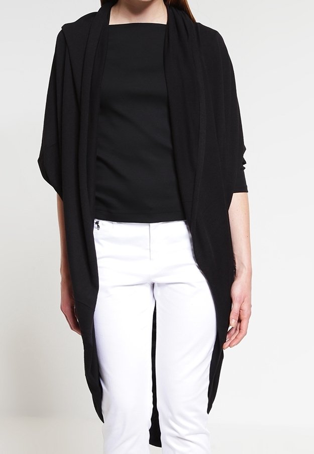 Svart öppen cardigan med långa ärmar, tillverkad av mjukt tyg, med en avslappnad passform och flödande design, bärs över en svart topp och vita byxor.