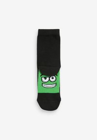 Svarta strumpor med en grön tecknad ansiktsdesign, som har en leende mun och stora ögon, med randiga texturer nära designen.