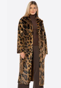 Kabát z umělé kožešiny s leopardím potiskem, který má dlouhý, rovný střih, široký límec a oversized rukávy, doplněný hnědým rolákem a kalhotami.