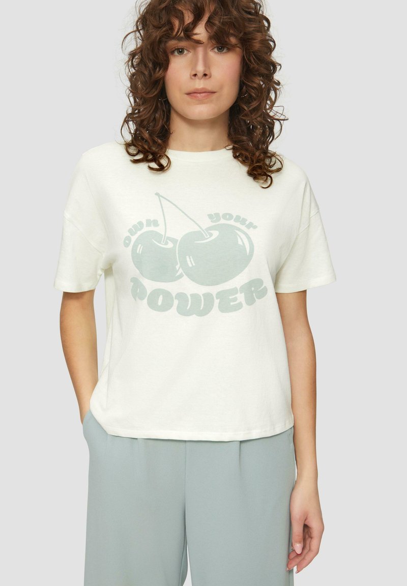 Crème-kleurige katoenen t-shirt met een losse pasvorm, waarop een grote groene kers graphic en de tekst "Own Your Power" in een speelse lettertype staan.
