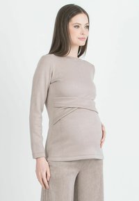 Top per maternità in beige morbido, con maniche lunghe e design incrociato in vita. Abbinato a pantaloni a coste beige coordinati.