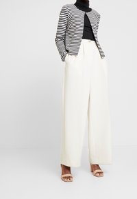 Mustavalkoinen raidallinen neuletakki mustan poolopaidan päällä, yhdistettynä korkeavyötäröisiin, leveälahkeisiin kreeminsävyisiin housuihin ja alastonvärisiin blokkikorkoisiin sandaaleihin.