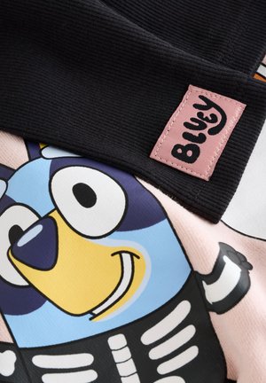 Must triibuline kangas roosa "Bluey" sildiga. Kujutatud on värvikas multikategelane sinise ja kollase näoga, kandes luustiku kostüümi.