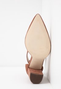 Brown suede high-heeled shoe with a pointed toe and a smooth sole. The heel is block-shaped with a textured bottom for grip.