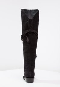 Botas de ante negras por encima de la rodilla con puntera redonda, cierre con cremallera en el lateral y detalle de hebilla ajustable en la parte superior. Textura suave.