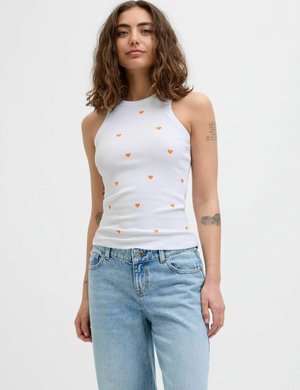Witte geribde tanktop met kleine oranje hartjespatronen, met een hoge halslijn. Gepaard met lichtblauwe, losse spijkerbroeken.