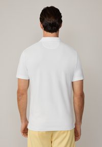 White polo shirt with a flat collar, short sleeves, and a textured surface. The back view shows a smooth finish and straight hemline.