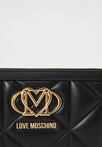 Clutch de couro sintético preto matelassé com um logotipo e ferragens em tom de ouro. Apresenta um fecho zip e padrões de costura diagonal.