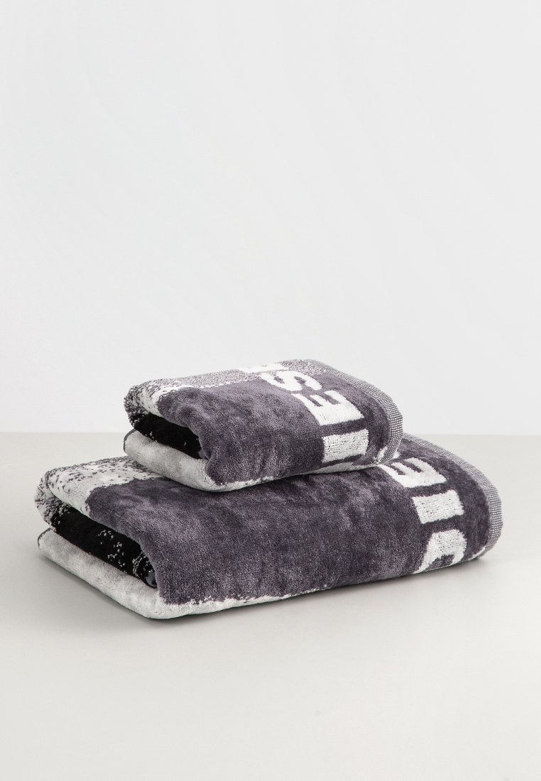 Serviettes grises et noires empilées, fabriquées en coton moelleux. La serviette plus grande comporte un texte blanc. La serviette plus petite a un bord texturé.