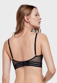 Soutien-gorge en dentelle noire avec bretelles réglables et fermeture à agrafes. Présente un dos en maille à motifs et une bande lisse pour un confort accru.