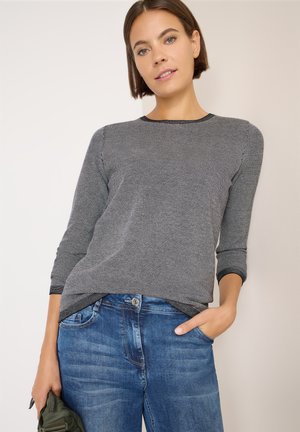 Suéter gris de manga larga con un patrón texturizado y acentos negros, combinado con jeans de denim azul. El suéter tiene un escote redondo.