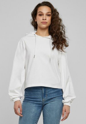 Hvit avkortet hettegenser med snøring, lange ermer med elastiske mansjetter, og en myk bomullstekstur. Kombinert med blå denimjeans.