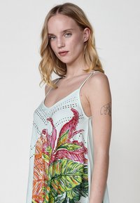 Lichtblauwe mouwloze jurk met grote bloemen- en bladerenprints in roze, oranje en groen, met een soepele textuur en een V-hals ontwerp.