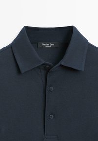 Dunkelblaues Poloshirt mit strukturiertem Stoff, Dreiknopf-Leiste und klassischem Kragen. Das Etikett trägt die Aufschrift "Massimo Dutti".