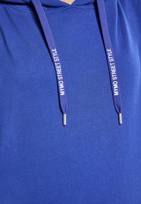 Felpa con cappuccio blu dal tessuto morbido. Presenta lacci scuri blu con la scritta "MYMO STREET STYLE" stampata in bianco. Terminali in metallo argentato sui lacci.