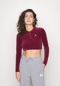 Polo burdeos de manga larga cortada en tejido de micropana con un pequeño logo Jumpman blanco. Combinado con pantalones de chándal grises con bolsillos.