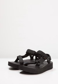 Mustat flip-flop-sandaalit, joissa on tekstuuriset kumipohjat, säädettävät nylon-hihnat ja litteä muotoilu. Minimalistinen tyyli, jossa on turvalliset kiinnitykset.