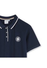 Tamsiai mėlynas polo marškinėlis su baltais akcentais, trijų mygtukų apykakle ir išsiuvinėtu logotipu. Trumpi rankovės su kontrastingo apdailos apykakle ir rankovėmis.