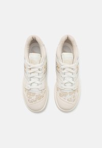 Paire de baskets beige et blanches avec lacets, vues de dessus sur un fond uni gris clair.
