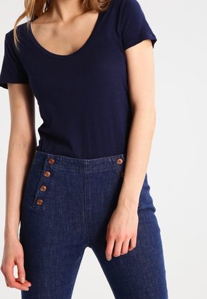 Granatowa koszulka z okrągłym dekoltem zestawiona z wysokim stanem ciemnoniebieskich dżinsów, z pięcioma brązowymi guzikami akcentującymi lewą stronę.