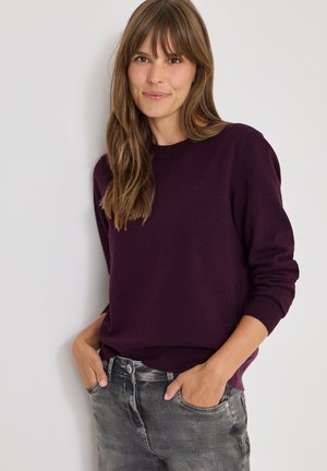 Maglione viola a collo tondo realizzato in morbido tessuto, con maniche lunghe e una vestibilità comoda, abbinato a jeans in denim grigi.