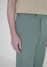 Pantaloni verde chiaro realizzati in tessuto morbido, caratterizzati da un design essenziale, gambe a taglio dritto e una semplice chiusura con bottone.
