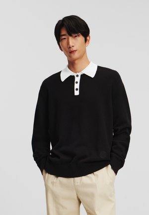 Pull en maille noire avec un col côtelé blanc et un plastron à quatre boutons. Présente une coupe décontractée et une taille texturée.