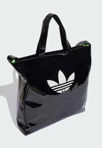 Black glossy tote bag with a white adidas trefoil logo and three parallel stripes; features green accent on top zipper.