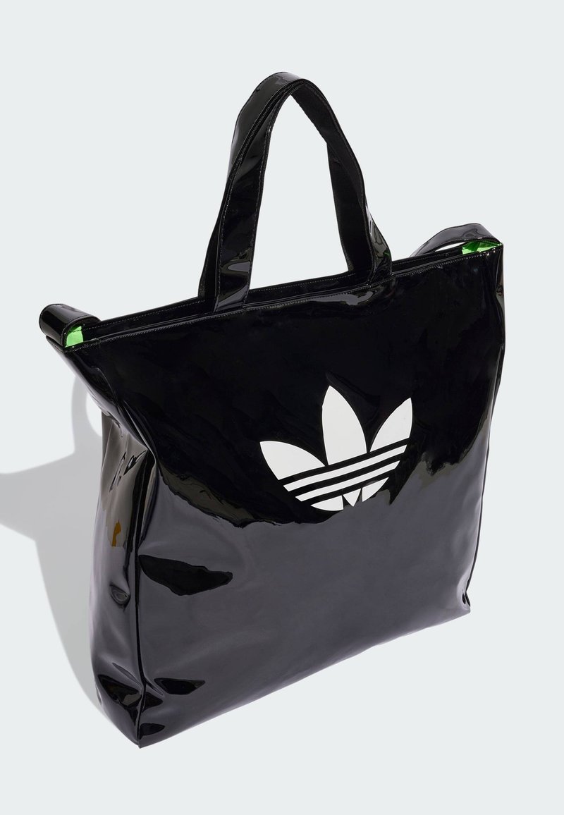 Bolsa de mano brillante negra con un logo de trébol blanco de adidas y tres franjas paralelas; presenta un acento verde en la cremallera superior.