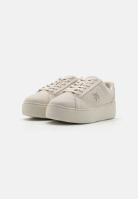 Beige sneakers with a smooth finish, round toe, thick platform sole, and flat laces. Features minimalistic logo detail on the side.