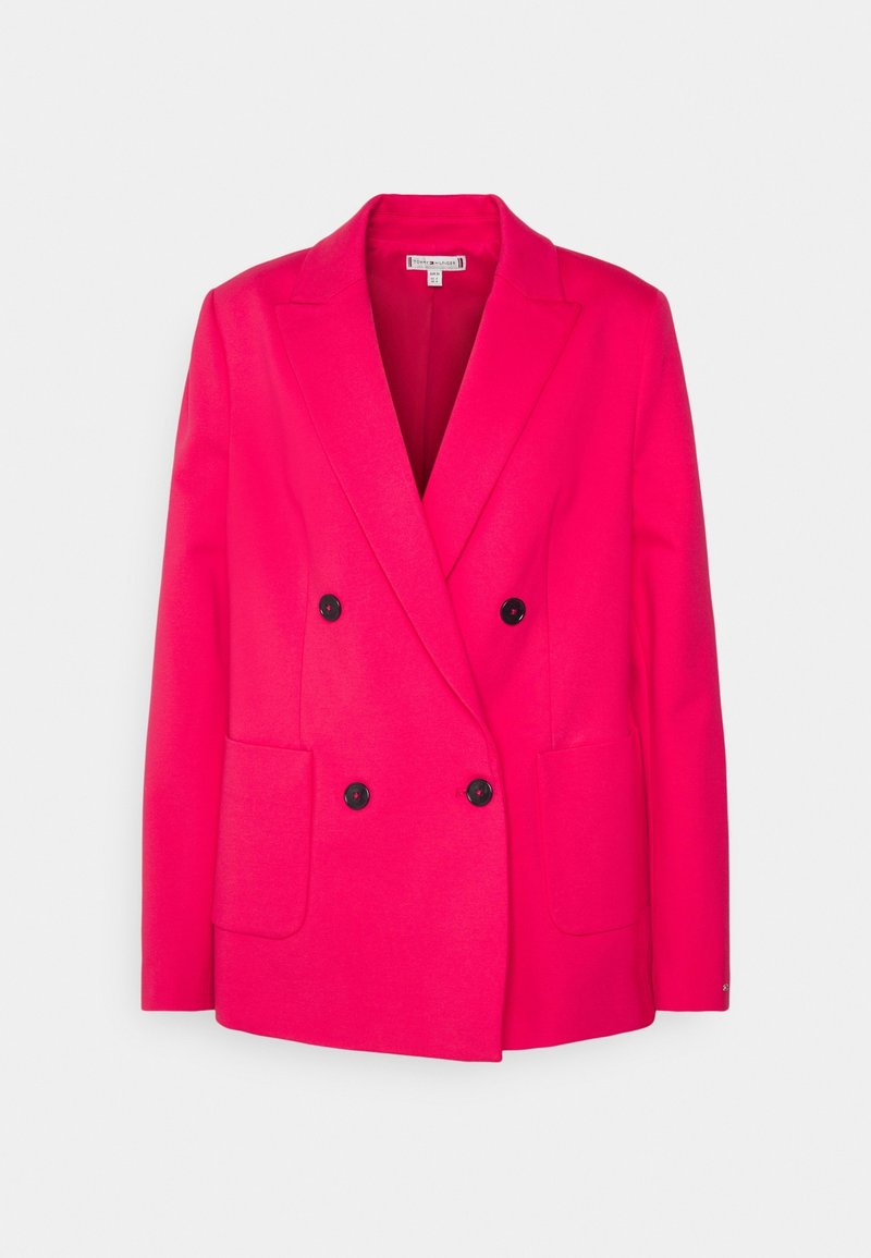 Blazer rose vif à double boutonnage avec boutons noirs, deux poches avant et col cranté ajusté, sur un fond clair.