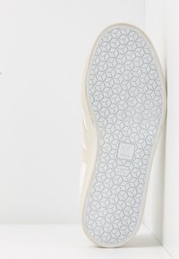 Baskets blanches avec des accents en suède beige. Semelle en caoutchouc texturée présentant un motif hexagonal. Logo intégré dans la semelle.