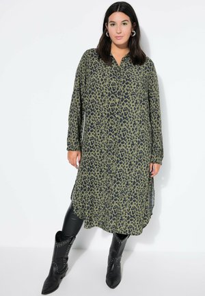 Olifijne groene shirtjurk met luipaardprint, lange mouwen en een knoopsluiting aan de voorkant. Gecombineerd met zwarte cowboylaarzen met studs.