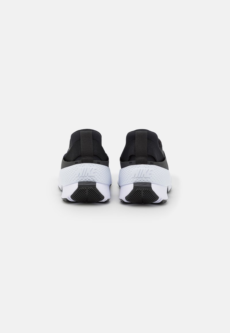 Zapatillas Nike en blanco y negro que presentan una parte superior de textura negra, un contrafuerte blanco con el logo y una suela de goma con patrones de tracción.