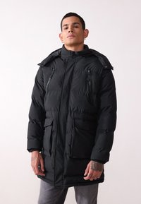 Chaqueta de plumas negra con cuello alto, cierre de cremallera y botones a presión, dos bolsillos frontales y capucha. Presenta una textura acolchada y un color sólido.