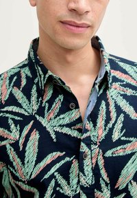 Camisa de manga corta en tejido azul marino con un patrón de hojas verdes y rosas, cuello clásico y cierre de botones con botones oscuros.