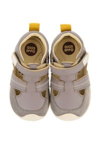 Zapatos de cuero y ante gris con puntera redondeada, lados recortados, correas de Velcro y una lengüeta amarilla en el talón. El forro interior es beige.