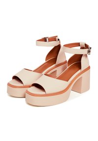 Beige plattform sandaler med en tjock blockklack, öppen tå, rem runt vristen och slät lädertextur. Har en kontrasterande sula.