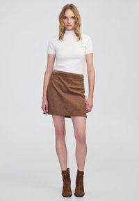 Top blanco de manga corta combinado con una falda mini de cuadros marrones. La modelo lleva botas de tobillo de ante marrón con un tacón grueso.