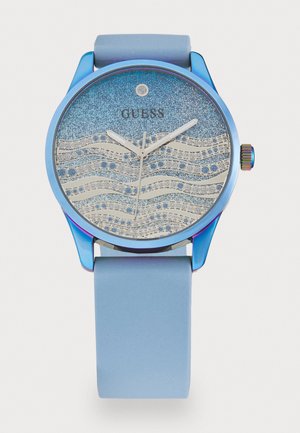 Montre avec un bracelet en silicone bleu et un cadran bleu pailleté présentant des motifs de vagues et des accents argentés. Aiguilles des heures et des minutes argentées, boîtier circulaire.