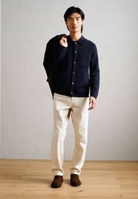 Σκούρο ναυτικό μπλε πουκάμισο με κουμπιά, μπεζ παντελόνι και καφέ υπόδηση. Λείο ύφασμα και μινιμαλιστικός σχεδιασμός με λεπτομέρεια τσέπης στο στήθος.